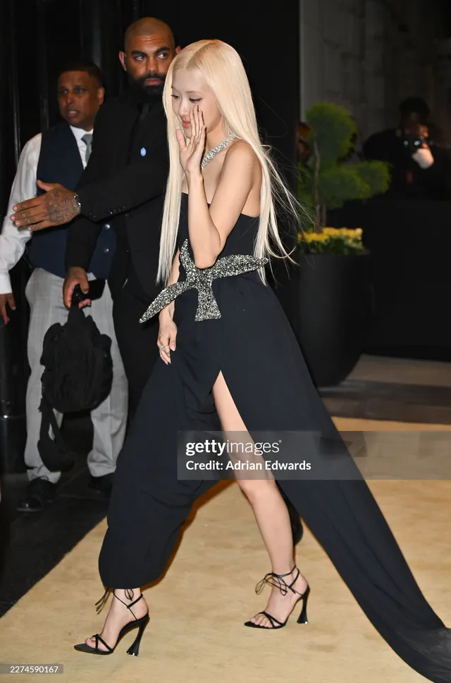 Rosé walking at an event in a long black dress and strappy high heels.