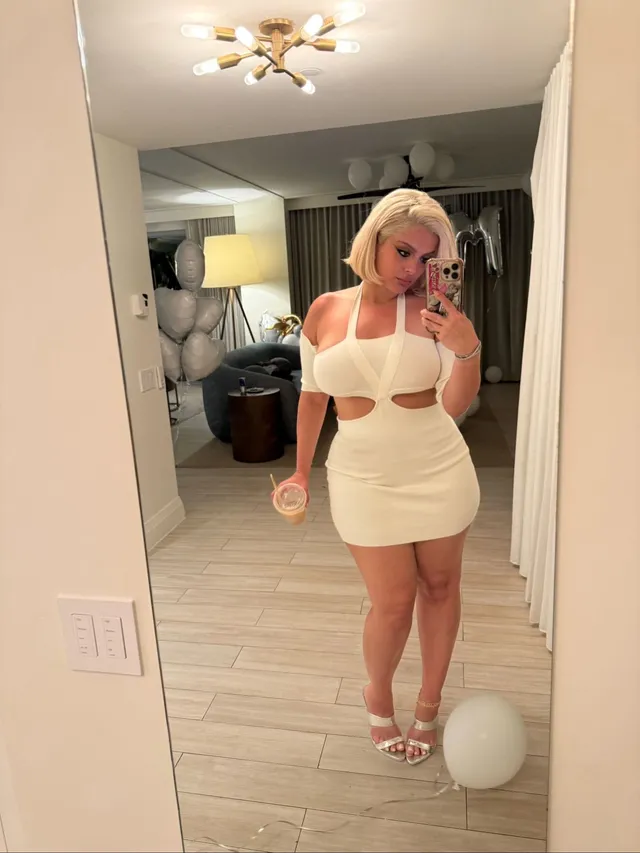 Bebe Rexha taking a mirror photograph in a white outfit and heels.