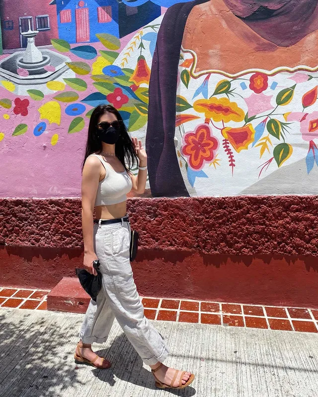 Adelaide Kane walking beside a colorful mural in flat sandals.