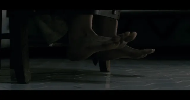 Eva Green showing bare feet beneath a chair in a dark film scene.