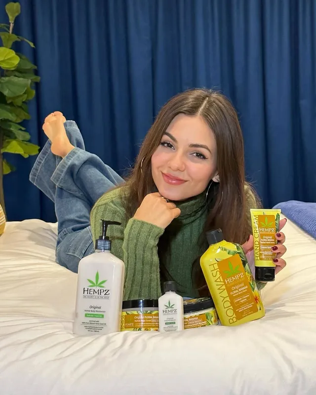 Victoria Justice lying on a bed beside skincare products.