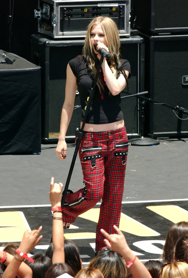 Avril Lavigne singing on stage in red trousers and flat sandals.