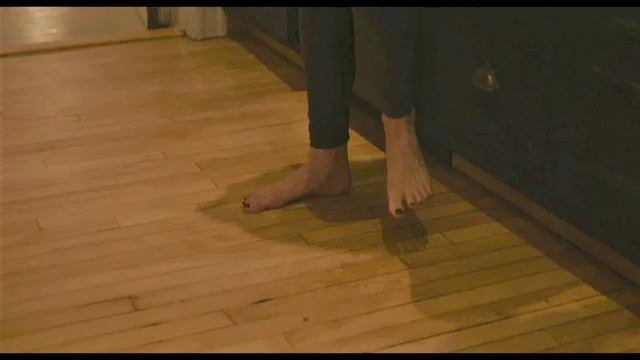 Vanessa Kirby a screen detail of bare feet on a wooden floor.