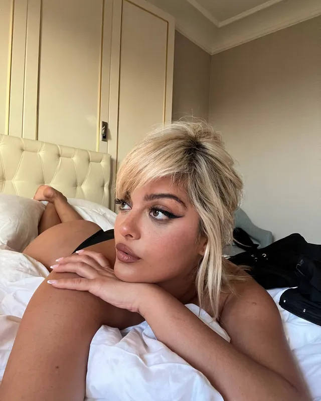 Bebe Rexha lying on a bed with bare feet raised behind her.