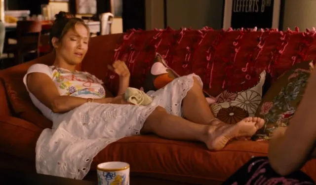 Jennifer Lopez a seated screen scene on a red sofa.