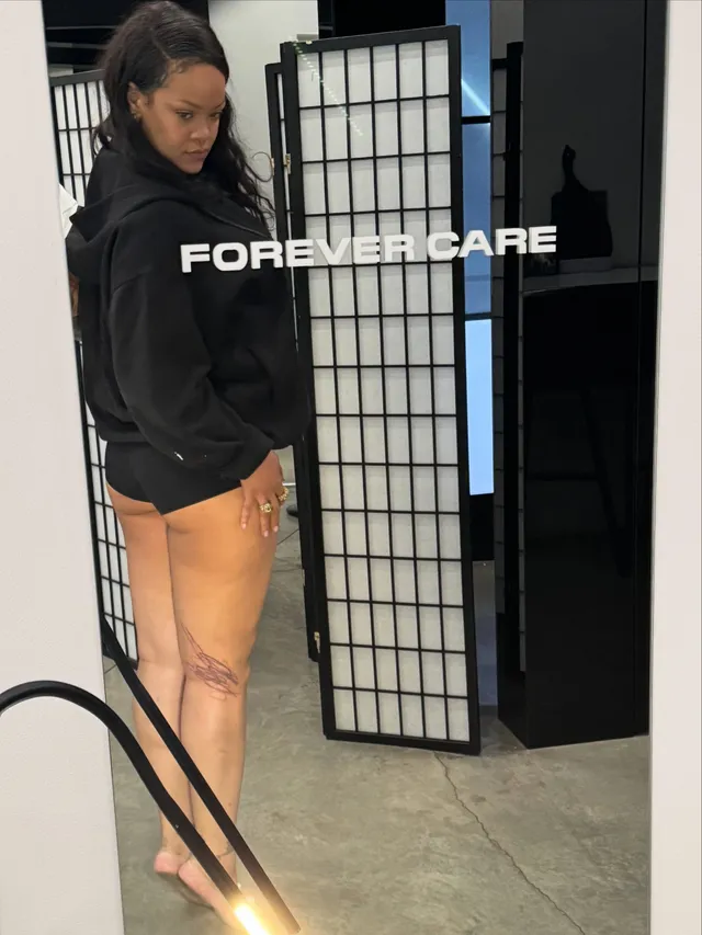 Rihanna standing indoors in a dark jacket and orange leggings.