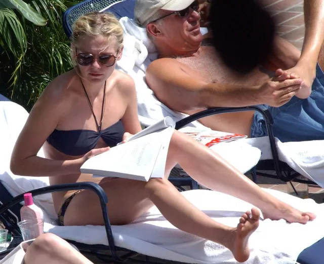 Kirsten Dunst sitting barefoot outdoors and reading beside another person.