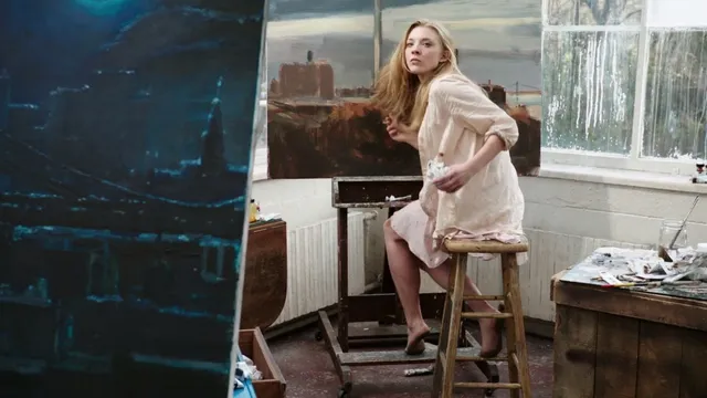 Natalie Dormer sitting on a stool in a pale outfit.