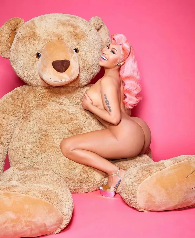 Nicki Minaj crouching beside a large teddy bear in clear heels.