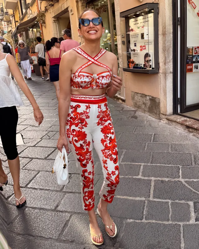 Jennifer Lopez a red patterned outfit and flip-flops on a city street.
