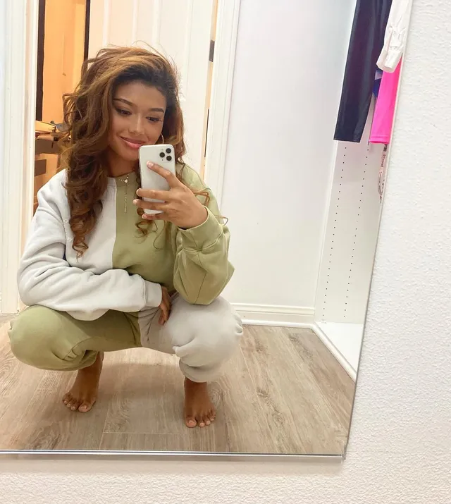 Sierra Capri taking a barefoot mirror selfie in a two-tone tracksuit.