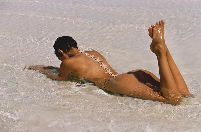 Taylor Hill lying barefoot in shallow water on a sandy beach.