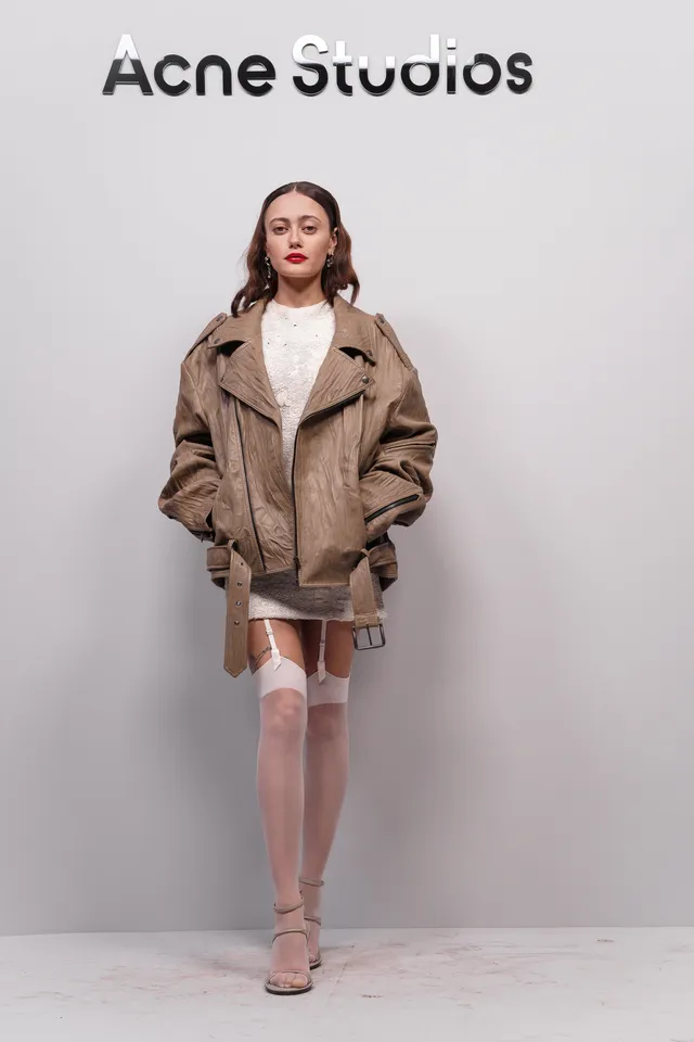 Ella Purnell posing at a fashion show in a brown coat.