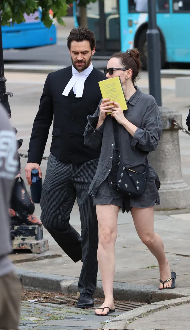 Daisy Ridley walking beside a man in a dark shirt and sandals.