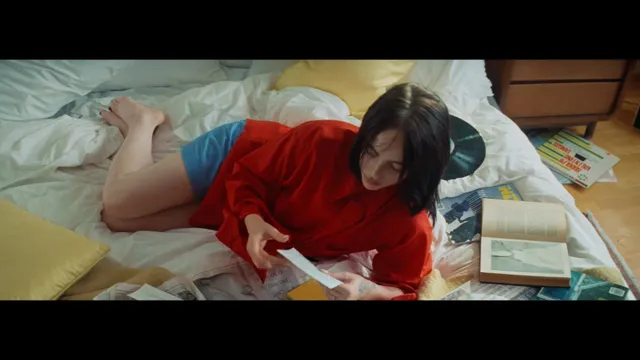 Billie Eilish a screen photograph in a red shirt on a bed.