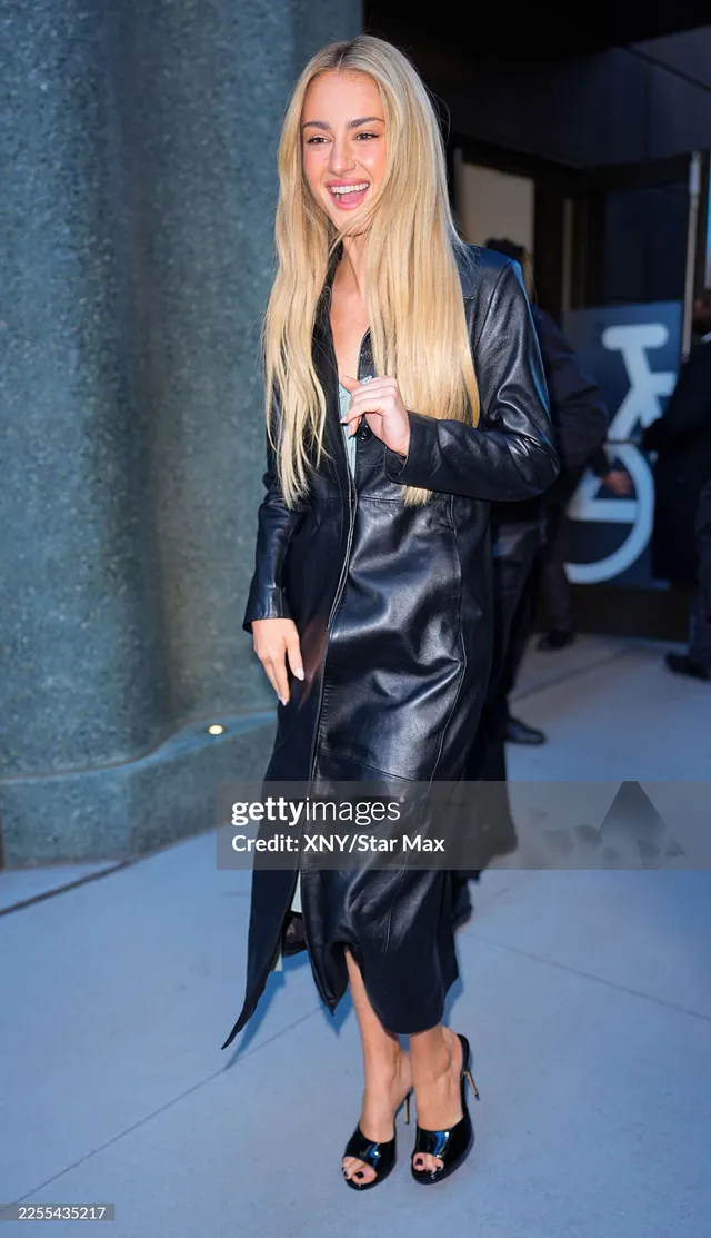 Grace Van Patten smiling outdoors in a black leather dress and heels.