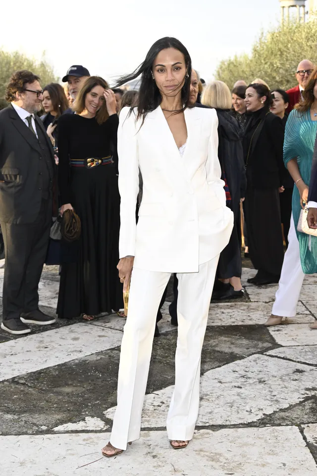 Zoe Saldaña standing at an event in a white suit.