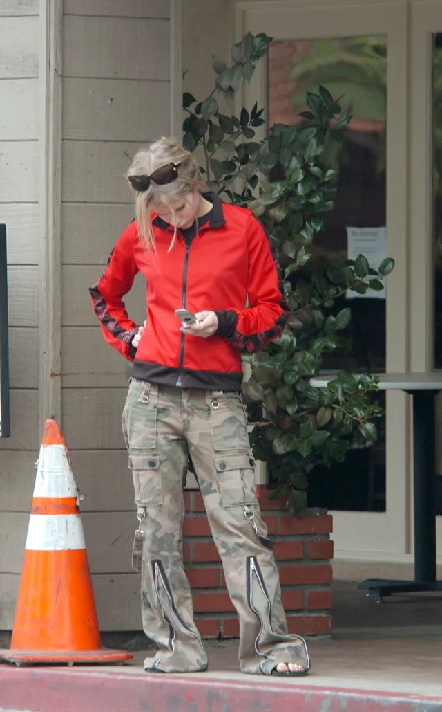 Avril Lavigne standing outdoors in cargo trousers and flip-flops.