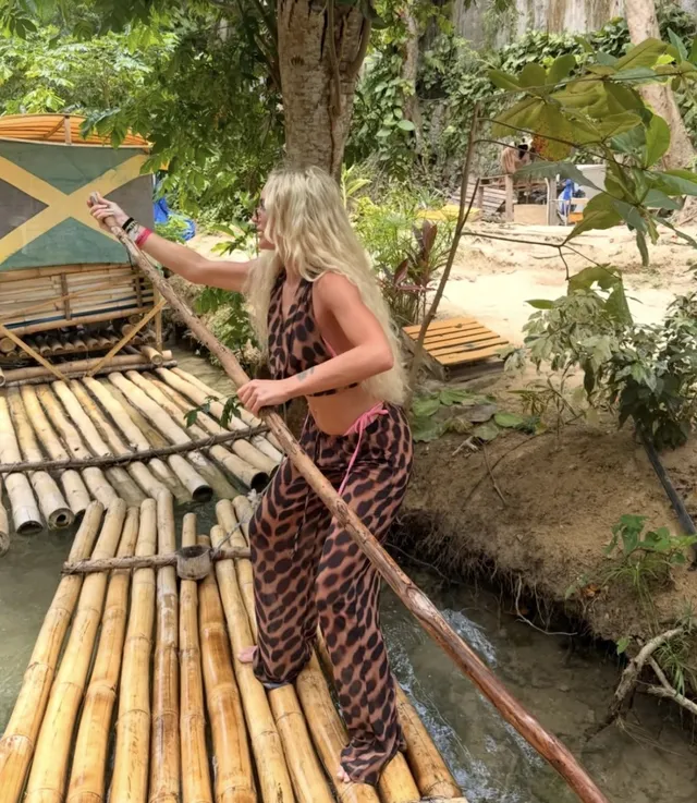 Alisha Lehmann walking on a bamboo platform in dark flat sandals.