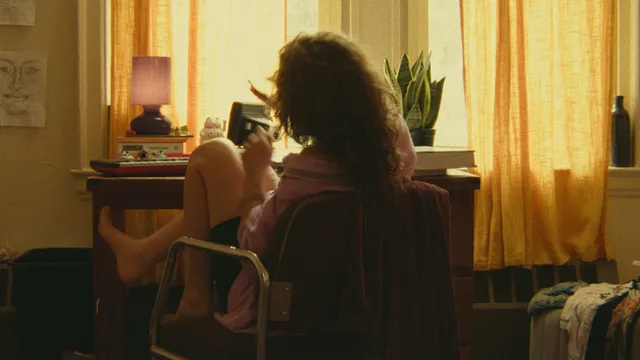 Odessa A'zion sitting barefoot on a chair by a window in a scene.