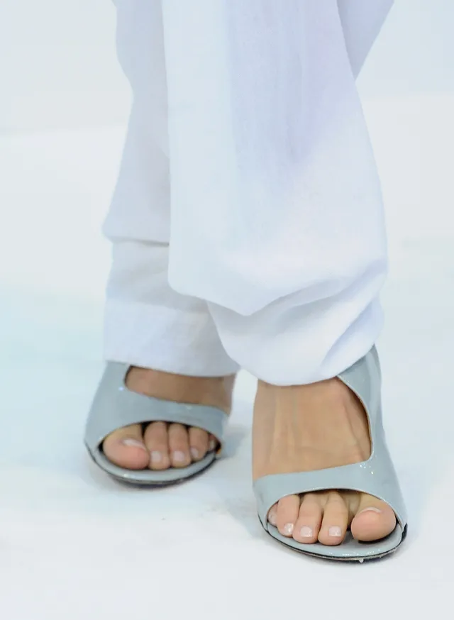Sienna Miller wearing pale blue mules beneath white trousers.