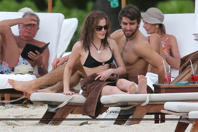 Emma Watson sitting barefoot on a beach lounger with friends.