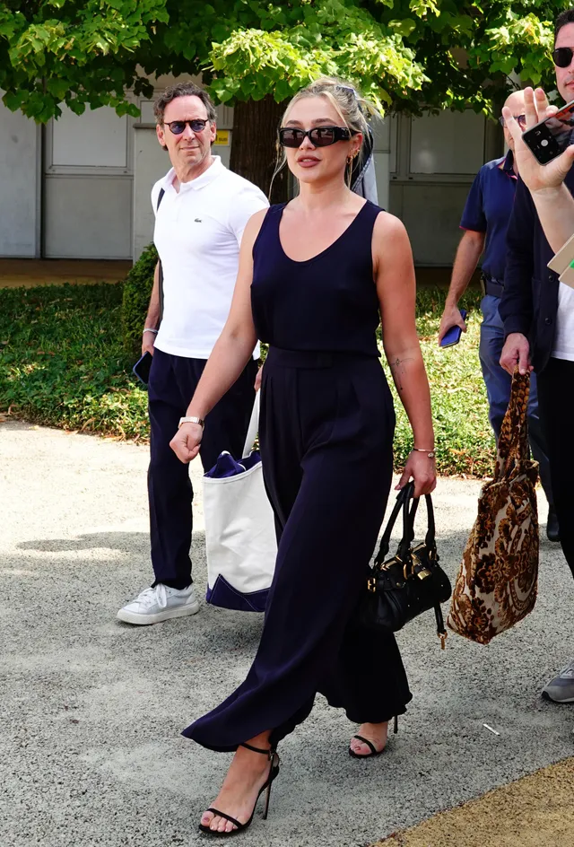 Florence Pugh walking in a dark jumpsuit and strappy heels.