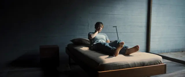 Kaley Cuoco reclining on a bed with her bare feet visible in a film scene.