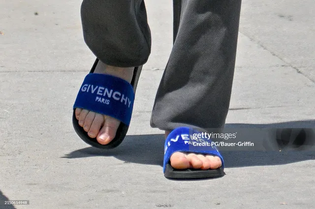 Kaley Cuoco wearing blue slides beneath dark trousers.