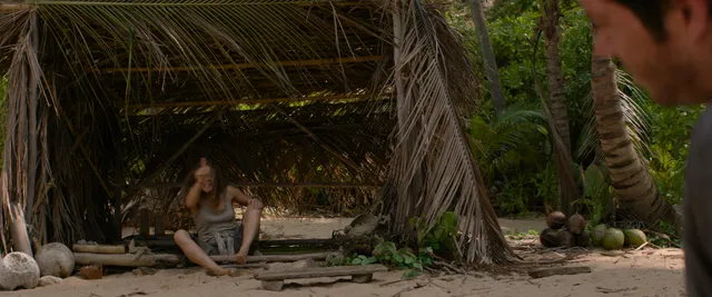Rachel McAdams moving barefoot beneath a tropical shelter in a film scene.