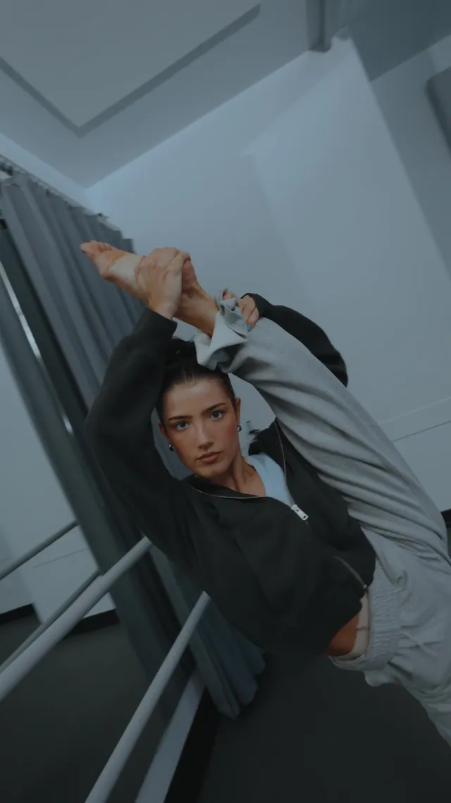 Charli D’Amelio stretching beside a ballet barre with a bare sole raised.