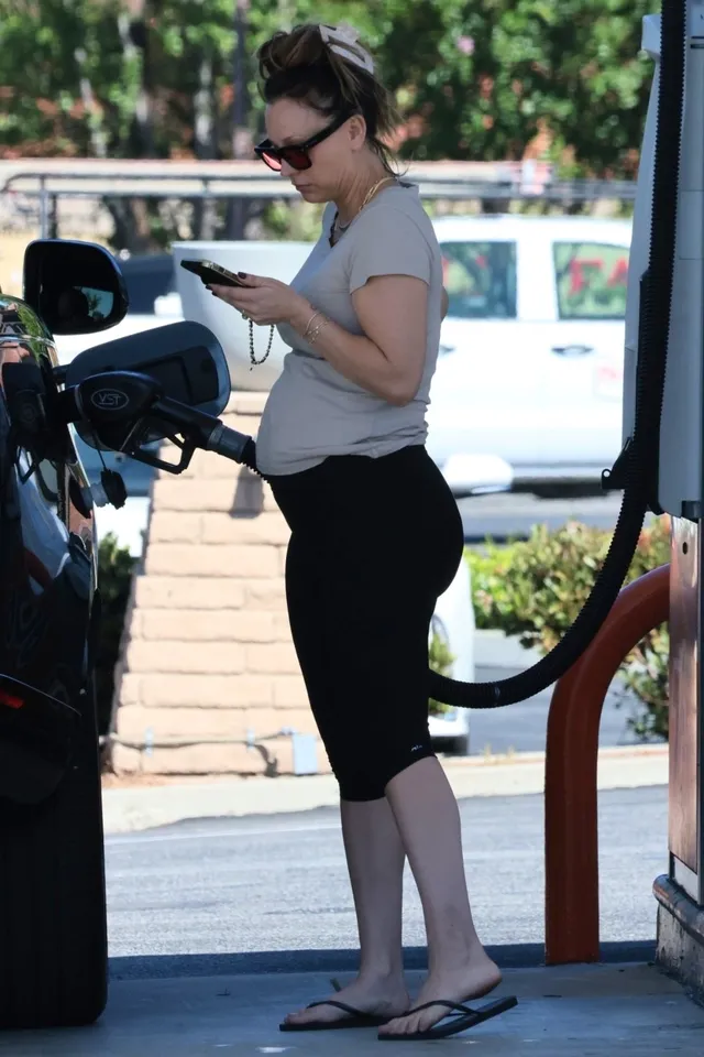 Kaley Cuoco standing beside a car at a petrol station in flip-flops.