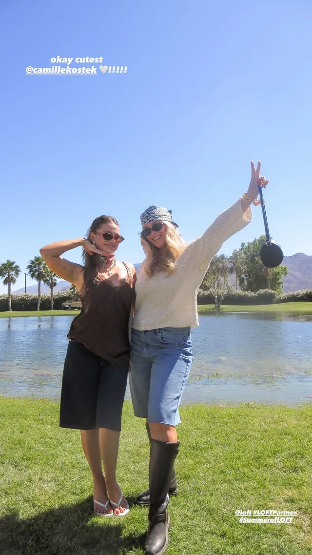 Olivia Holt posing with a friend on grass in a dark outfit and sneakers.