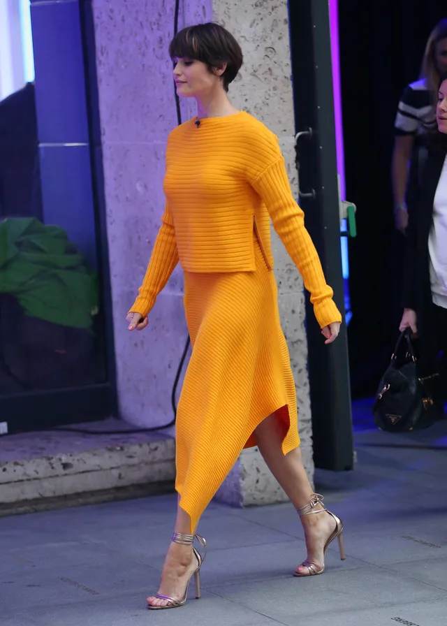 Gemma Arterton walking outside in a yellow dress.