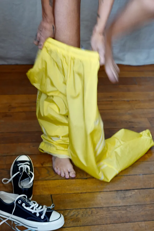 Miley Cyrus standing barefoot beside trainers in a yellow outfit.