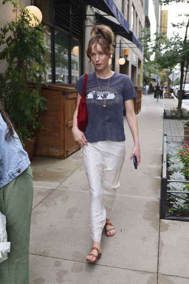 Jennifer Lawrence standing outdoors in a T-shirt and flat sandals.