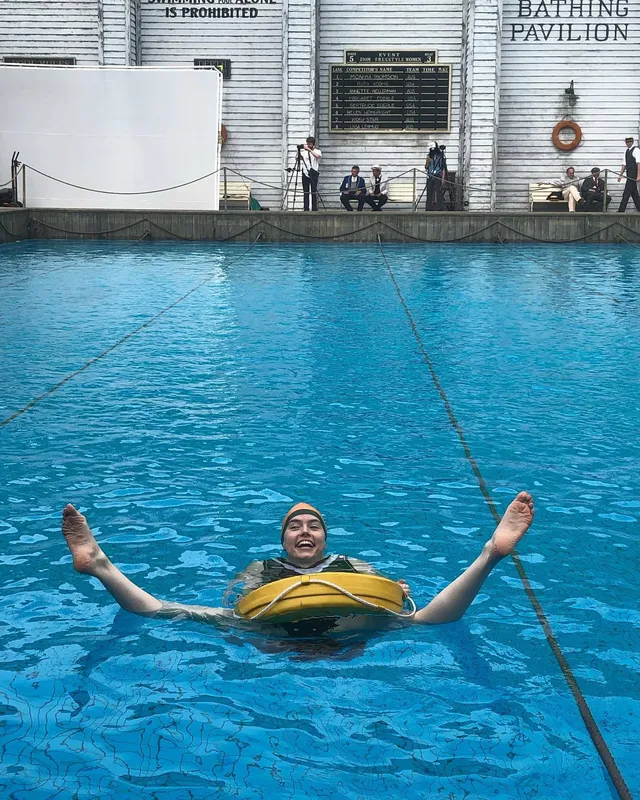 Daisy Ridley floating in a swimming pool with her feet raised.