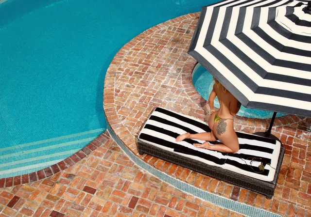 Iggy Azalea sitting barefoot on a striped lounger beside a swimming pool.