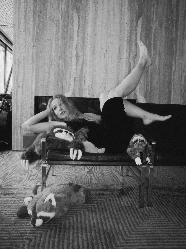 Kristen Bell reclining barefoot on a sofa beside dogs in a black and white photograph.