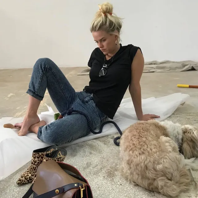 Alice Eve sitting on a bed beside a dog.