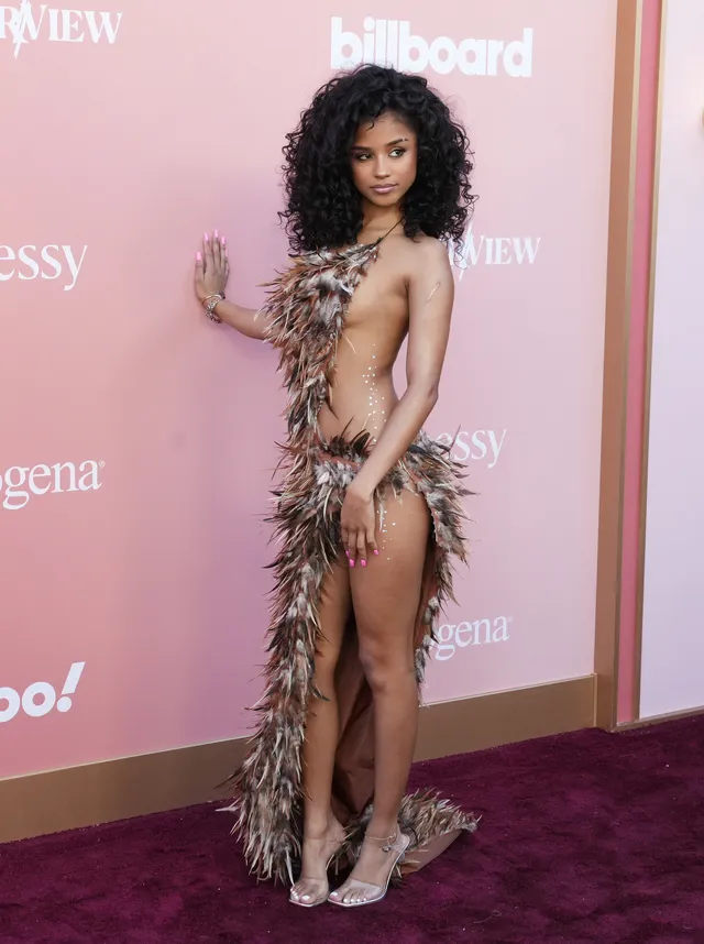 Tyla wearing clear heels and a feathered dress on a pink carpet.