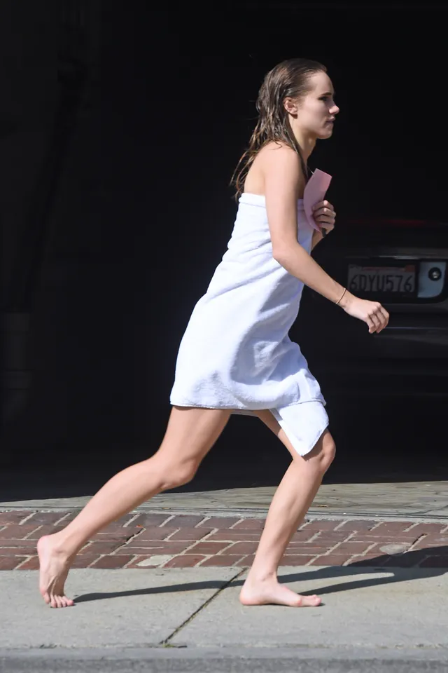 Suki Waterhouse walking outside wrapped in a towel.