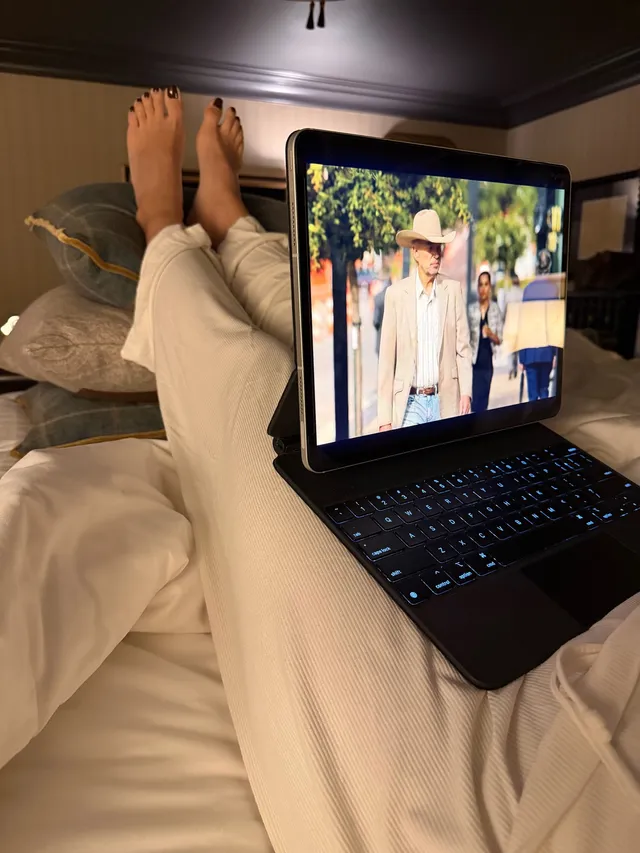Shay Mitchell resting with a laptop and bare feet on a bed.