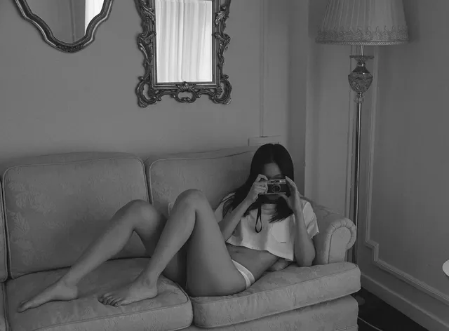 Jennie Kim reclining barefoot on a sofa in a monochrome indoor photograph.