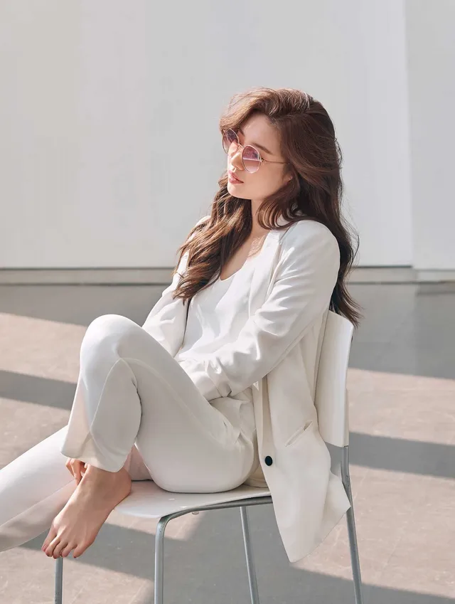 Bae Suzy posing barefoot on a chair in a white suit.