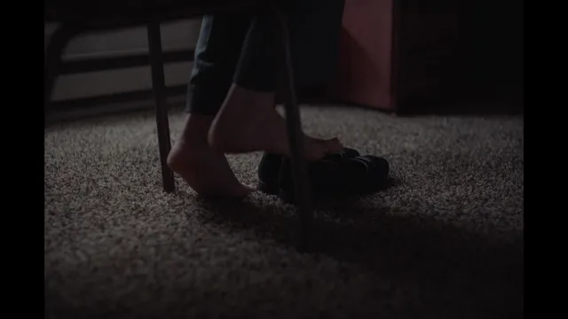 Daisy Ridley standing on a carpet in a dimly lit screen scene.