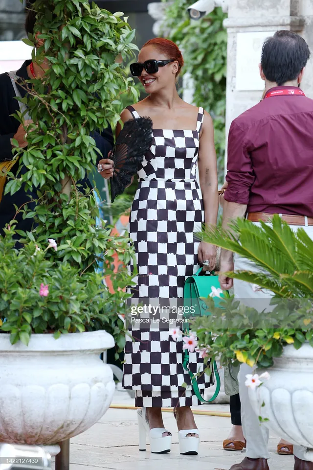 Tessa Thompson standing among greenery in a checked dress.