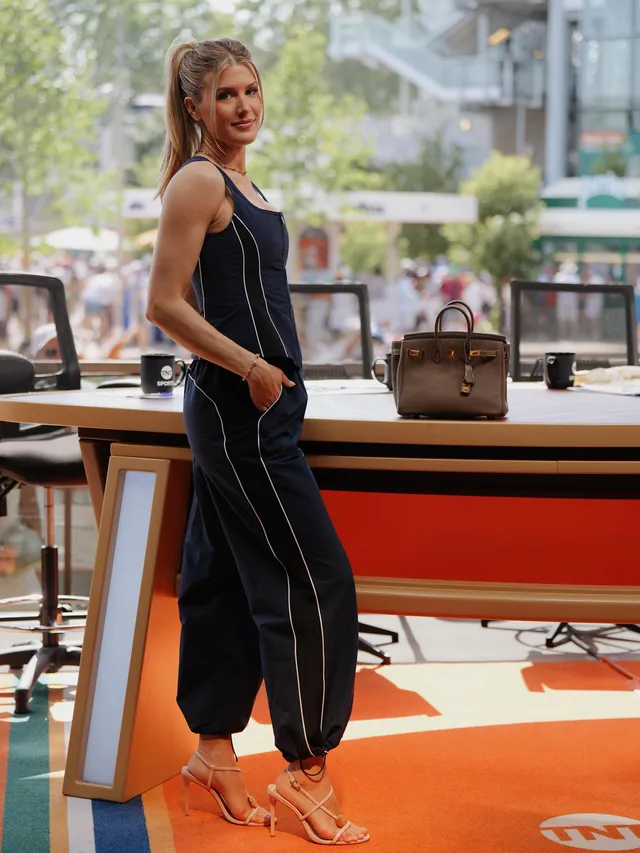 Eugenie Bouchard standing in heeled sandals and a dark sleeveless outfit at a sports venue.