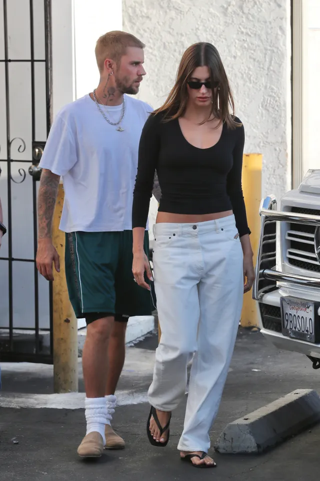 Hailey Bieber walking in white jeans and casual sandals.