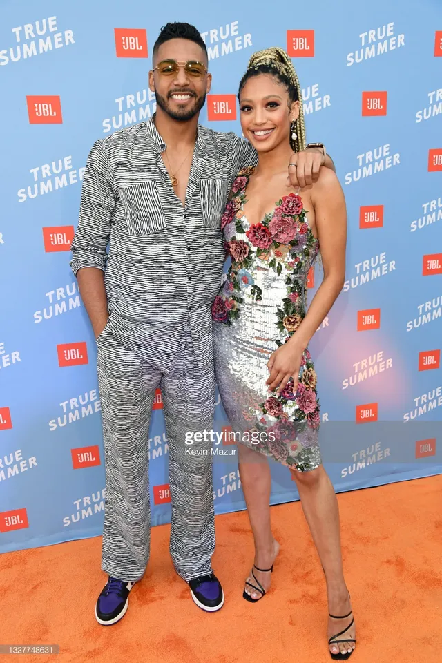 Samantha Logan posing beside a man in a floral dress and black heels.